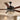 Black Queen ceiling fan with four dark brown wooden blades and an ornate black metal motor housing, featuring a hanging crystal chandelier light below. The fan is shown installed on a beige ceiling in a modern home interior.