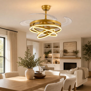 Luna ceiling fan light fixture with a brushed gold metal frame and white curved blades, installed in a bright, contemporary living room with a wooden dining table in the foreground.